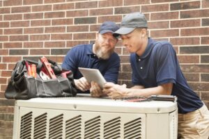 Two technicians diagnosing an issue on top of an air conditioner cabinet.